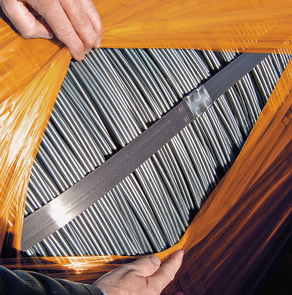 Steel rods completely wrapped in BioCor® corrosion protection film. Two overlapping layers of film are pulled apart by one person, revealing the steel rods.